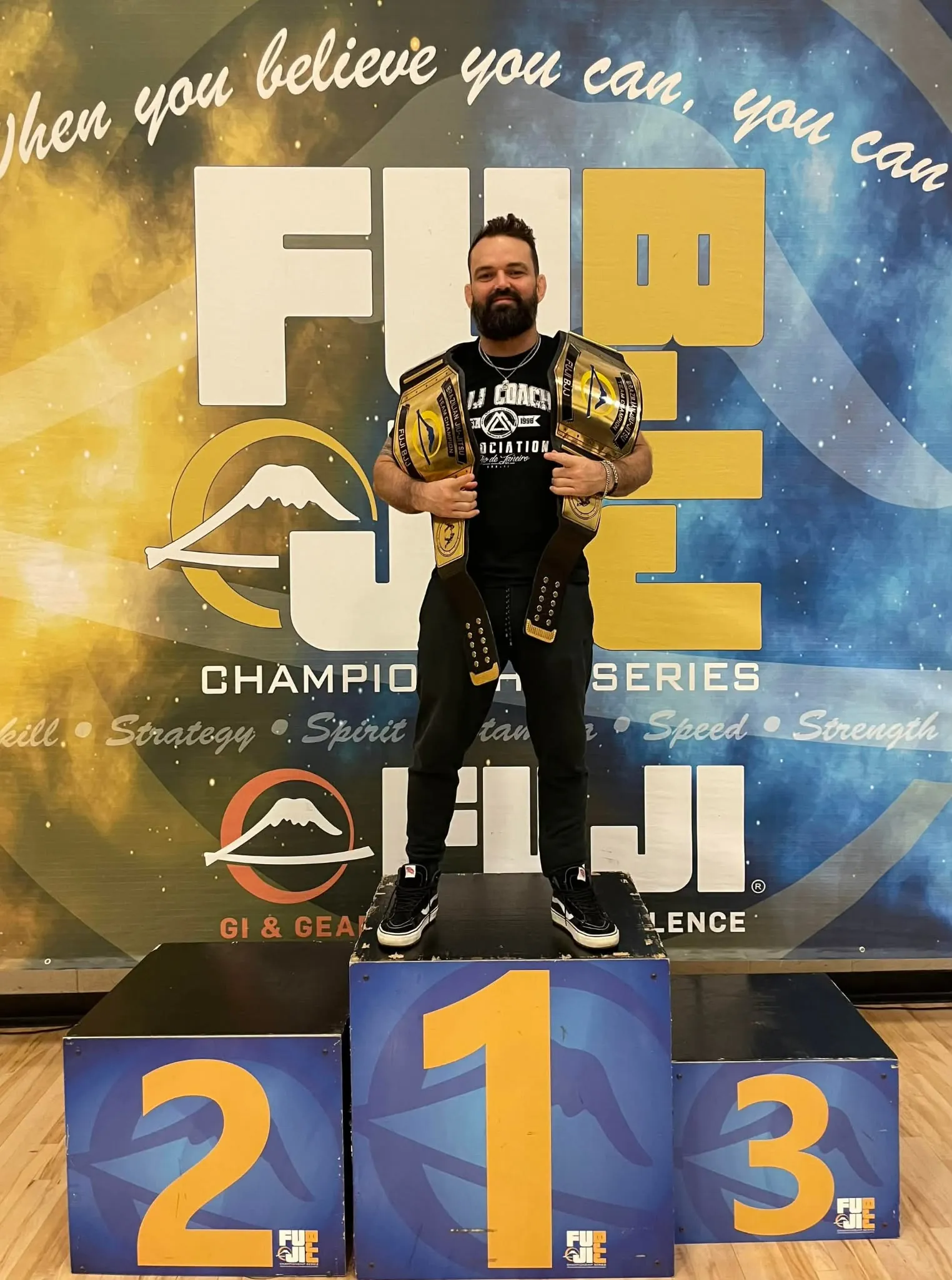 Coach Jon Correa on the podium with two championship belts