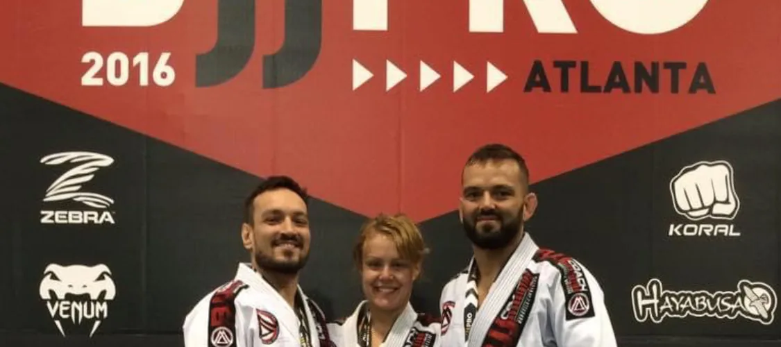 A woman wearing a gold medal on a tournament podium between two teammates in white gis